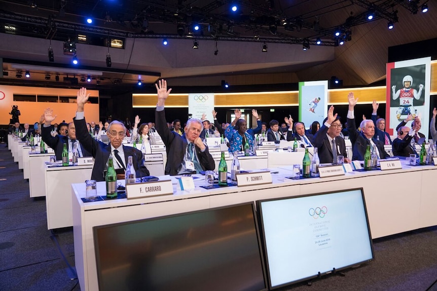 Several officials raises their hands at a meeting of the International Olympic Committee in Switzerland