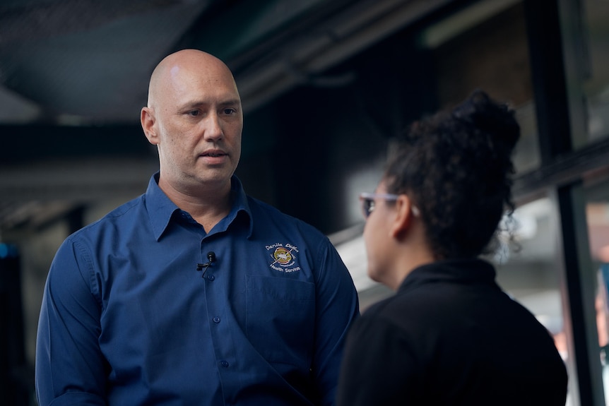 Bald man in blue shirt talks to woman in front of him