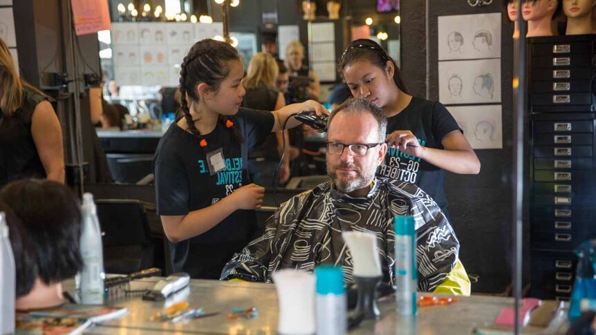 Two schoolgirls cut the hair of a man.