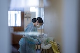 A nurse standing in a hospital hallway pulls off her shower cap while dressed in full PPE 