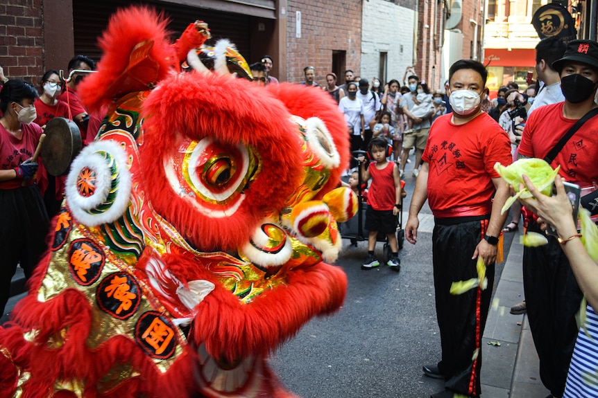 A chinese dragon on a street with a crowd behind it, wearing masks