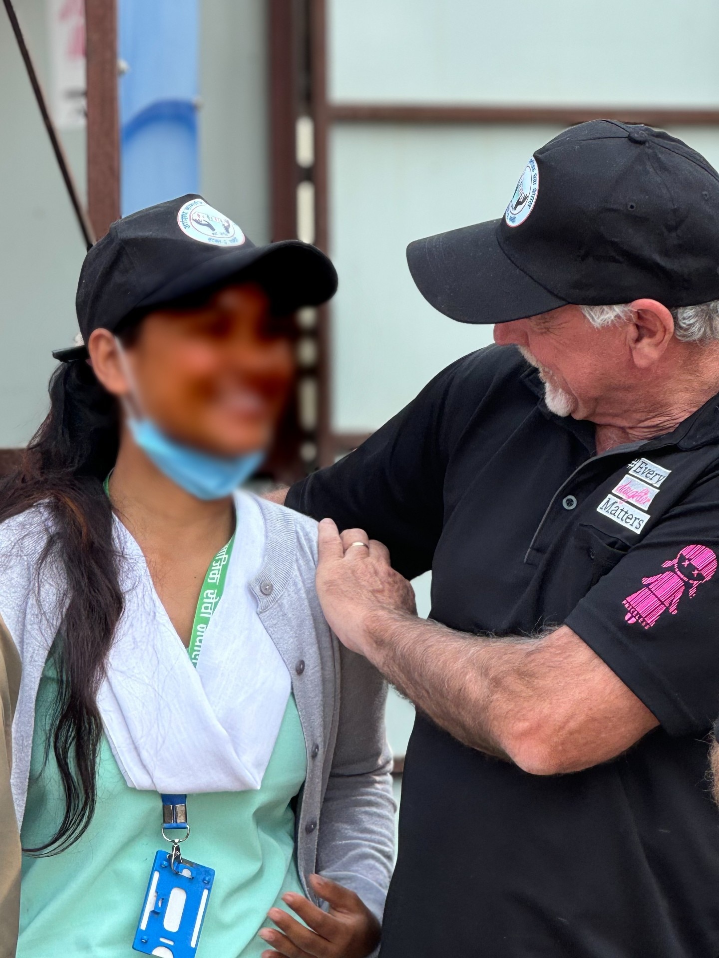 Uma jovem nepalesa com um uniforme azul-marinho e branco e seu rosto desfocado com um homem vestindo uma camiseta preta 