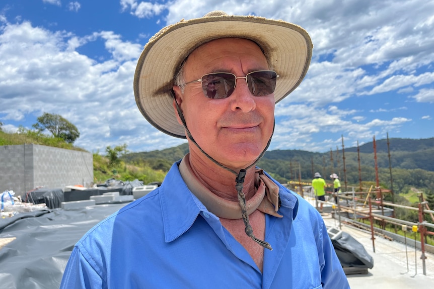 Tony Crockett looks at camera, wearing hat and sunnies at a construction site. 