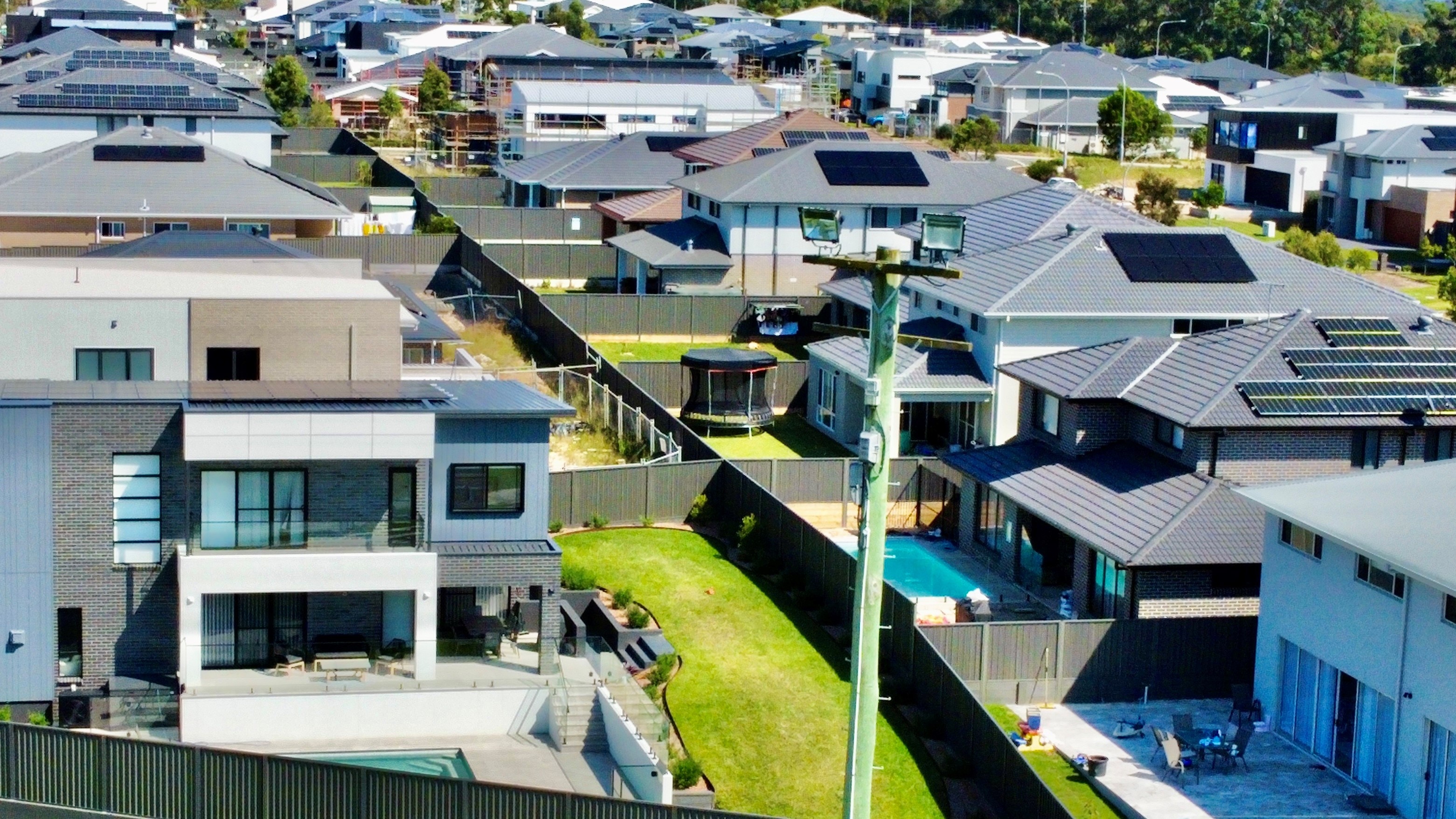 An aerial view of backyards of houses in a new housing estate with pools and green lawns.
