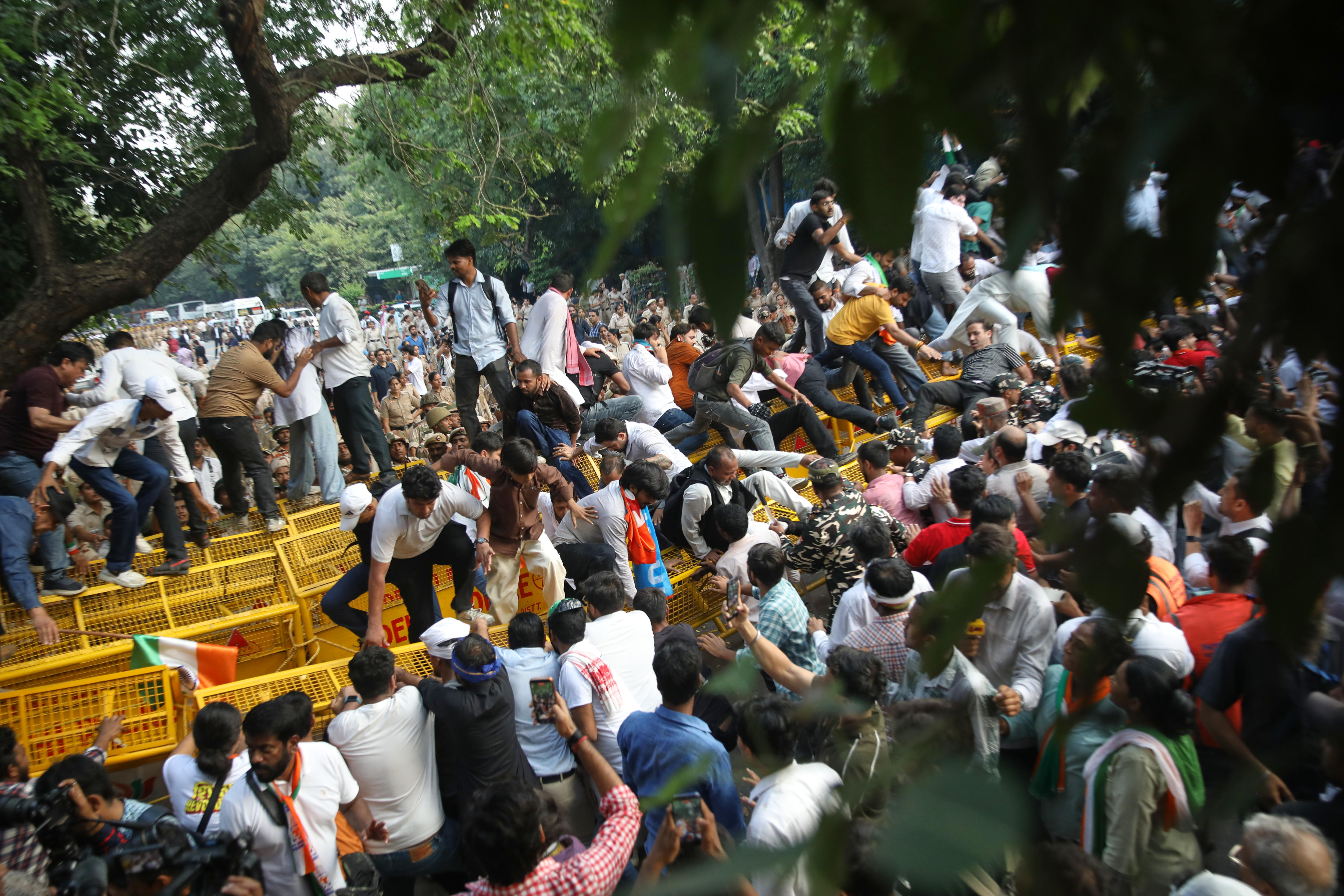 Dozens of people climb over yellow metal fencing.