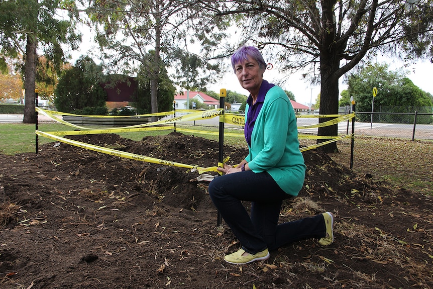 A woman kneels at an excavation site in school grounds