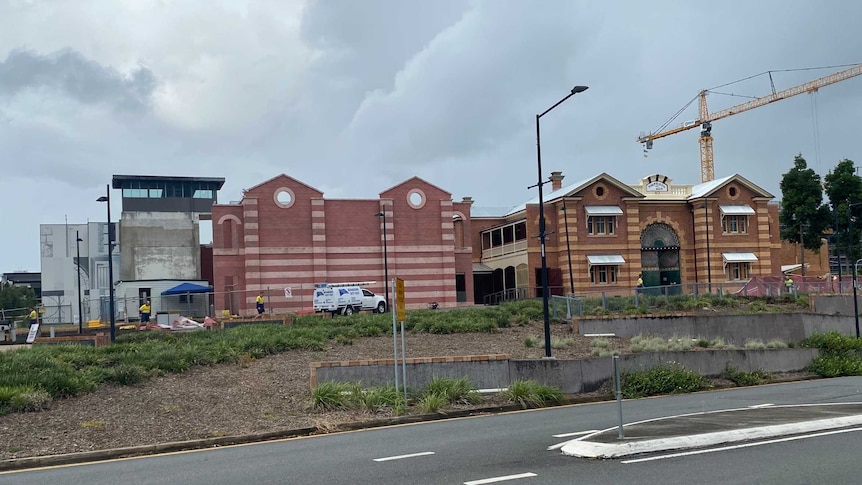 A red and yellow brick building from the 1880s stands with cranes behind it.