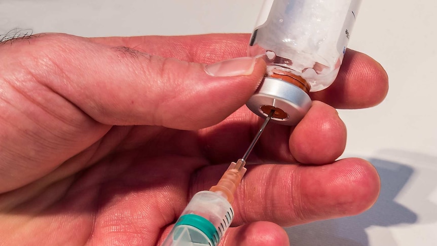 A close-up of a needle drawing fluid out of a bottle