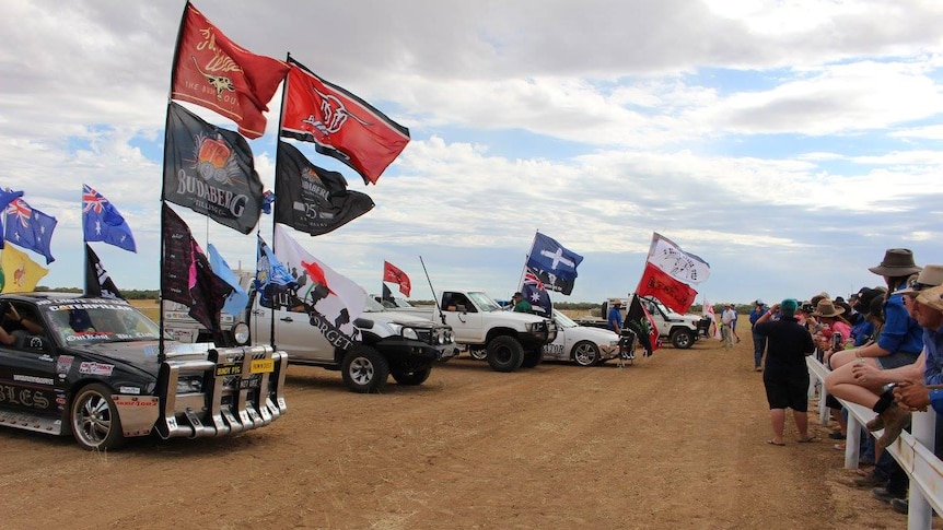 Cars with flags line up on desert road