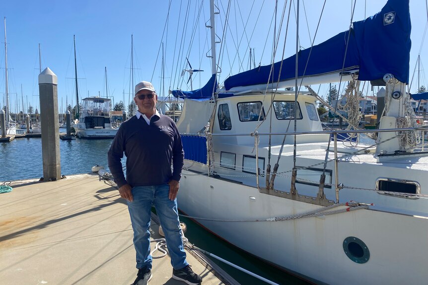 A man standing in front of his boat docked in a marina.