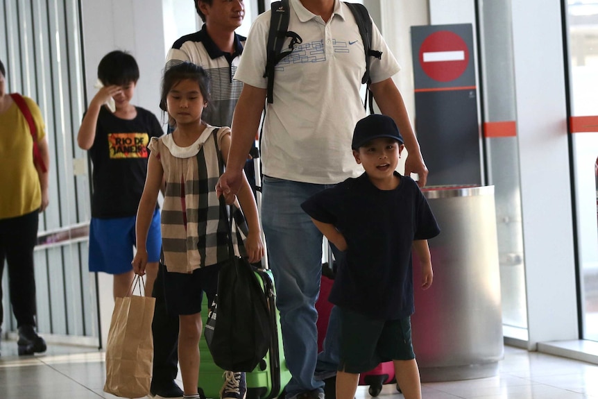 A little boy  smiles as he walks through the airport gates, a little girl walks behind him along with two adults.