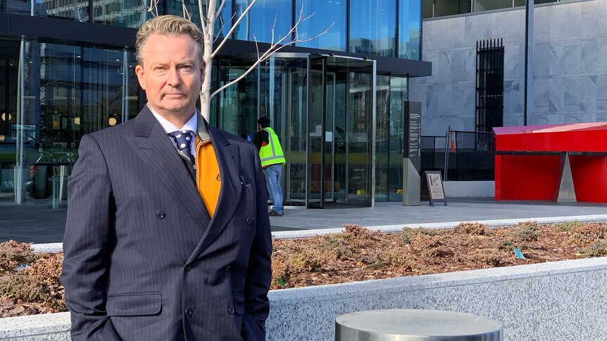 A man in a suit stands outside a courthouse.