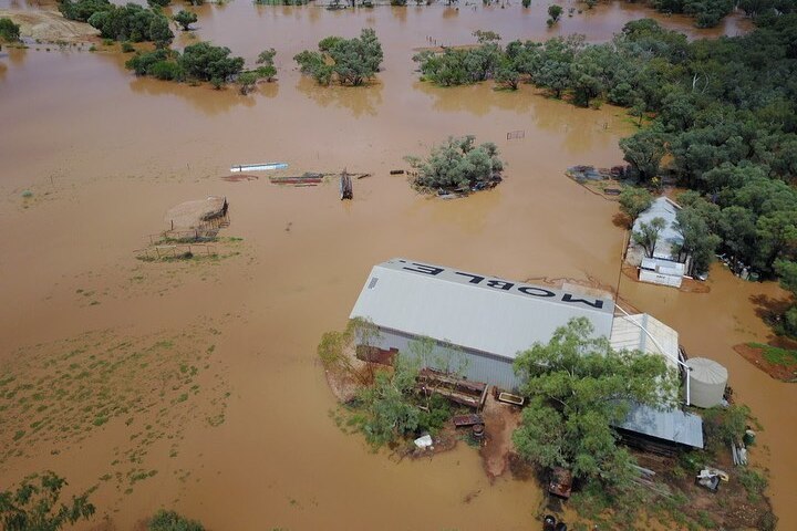 Brown floodwater surrounds a big tin building with MOBLE written on the roof.