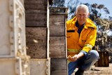 A man in a yellow jacket squatting next to beehives
