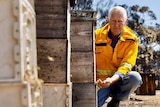 A man in a yellow jacket squatting next to beehives