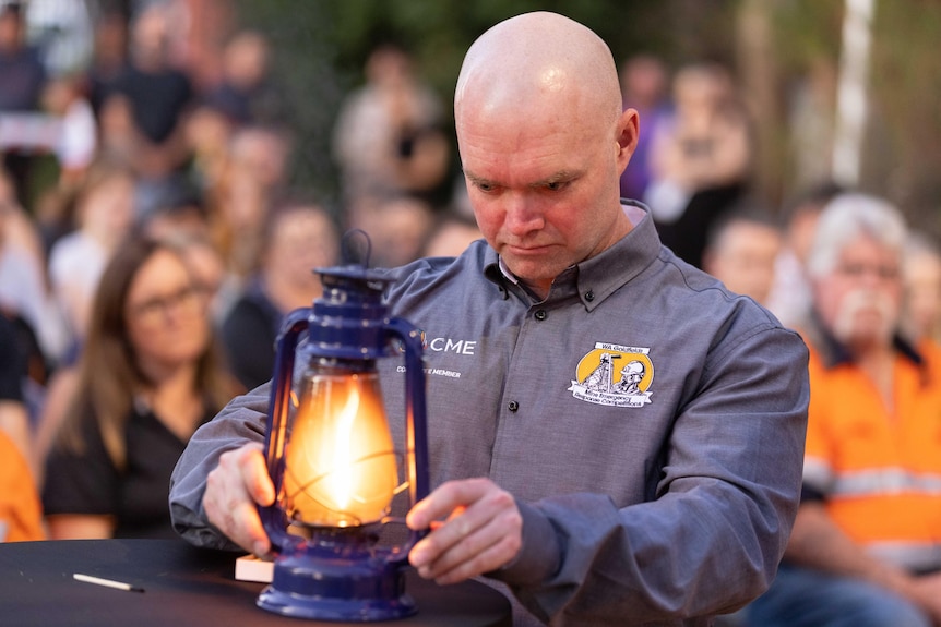 A man lighting a miner's lantern at a memorial service.  