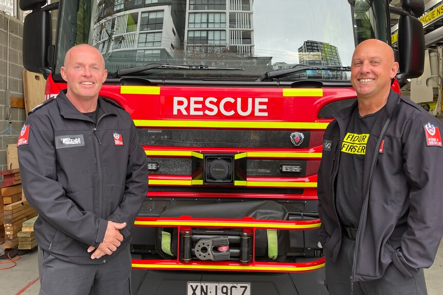 Two bald men standing in front of firetruck