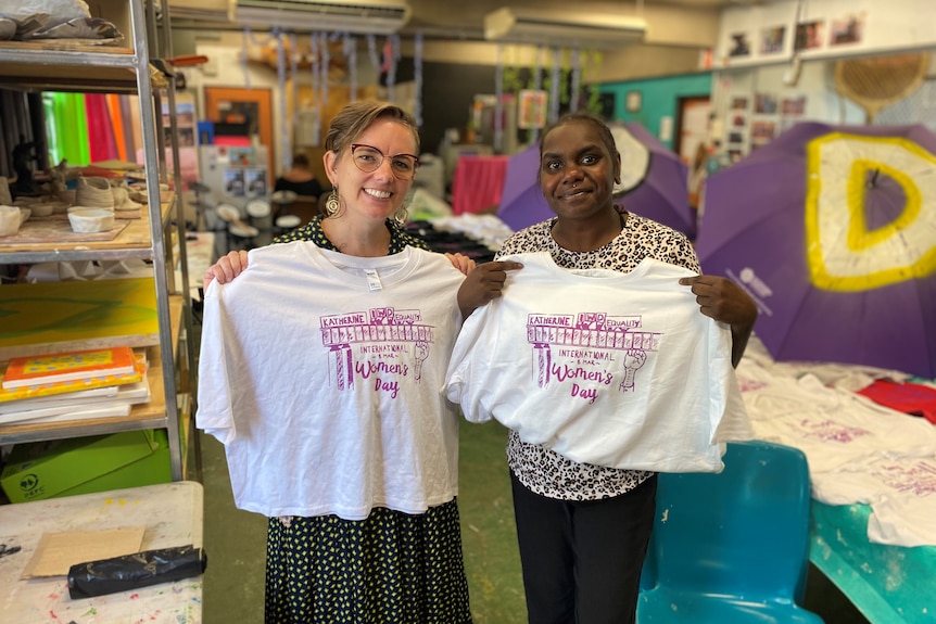 two women holding t shirts with purple designs on them