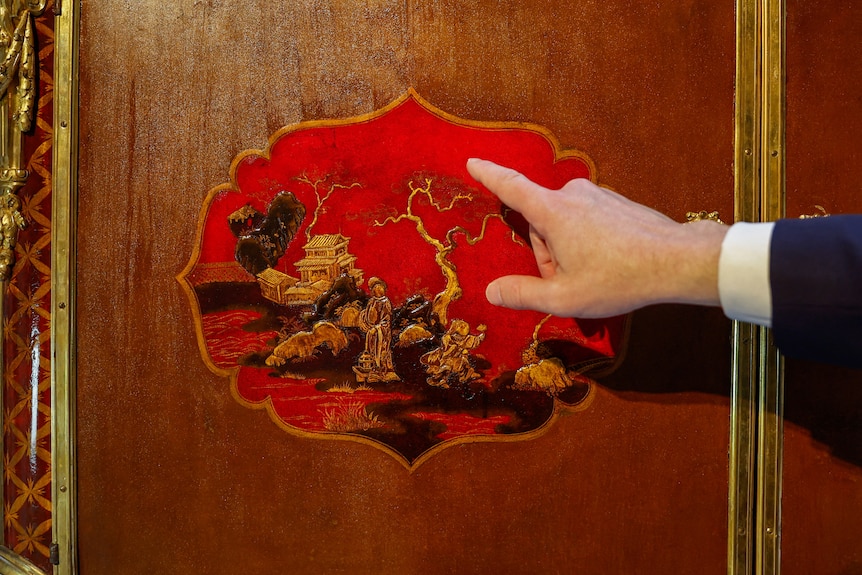 A painted Chinese-inspired design on wood as a man's hand points at it. 