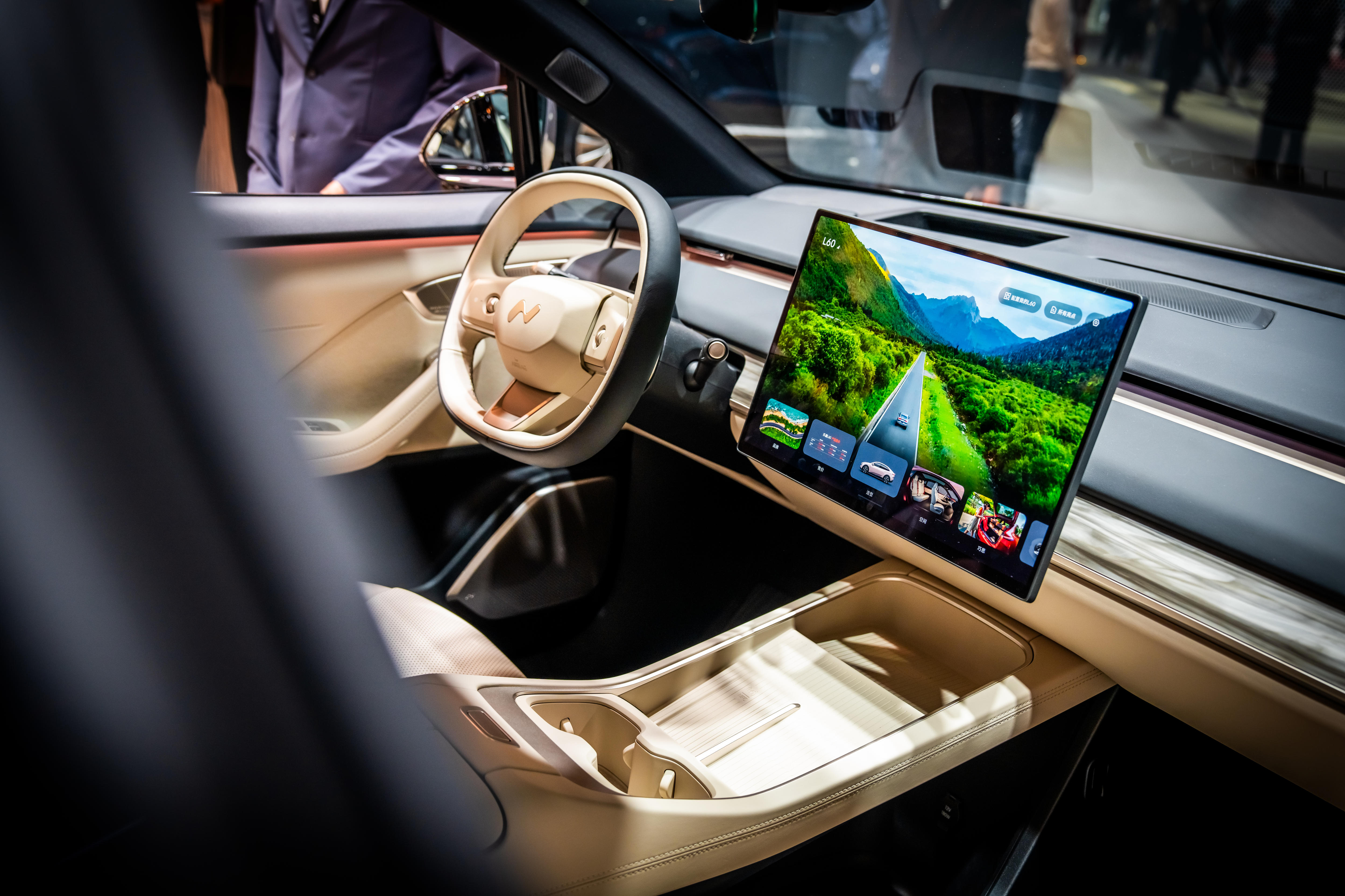 The inside of a luxurious electric vehicle with cream leather seats and a large screen