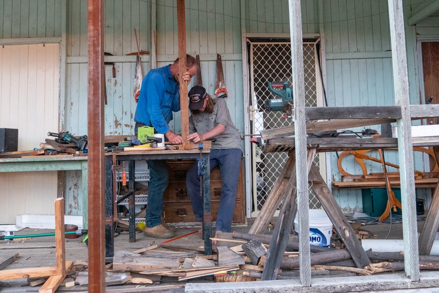 Dom and his dad fixing pieces of timber together on the verandah of an old farm house, near Longreach, November 2022.