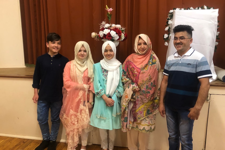 Man, woman, 2 girls and a boy wearing Afghani traditional dress, stood together and smiling. 