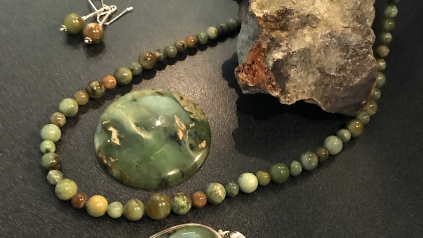 Green gemstone  jewellery on a bench next to the gemstone in its original rock form
