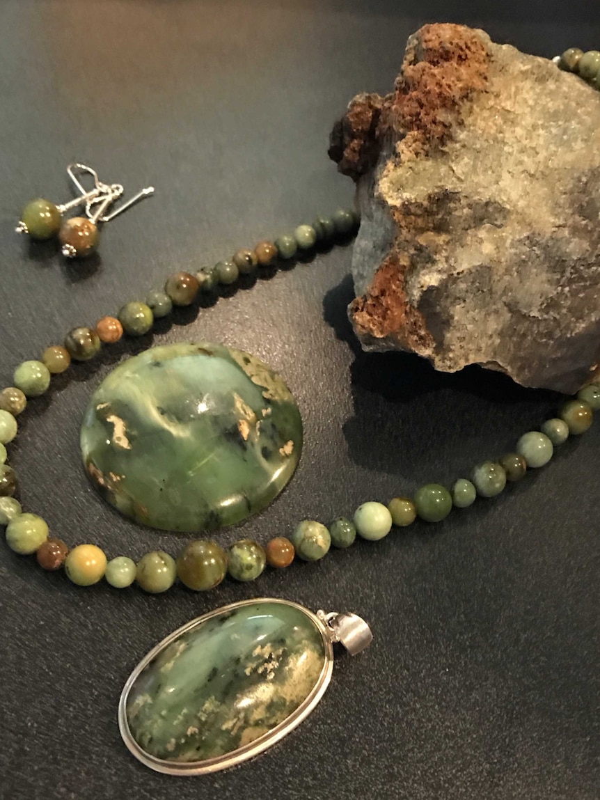 Green gemstone  jewellery on a bench next to the gemstone in its original rock form