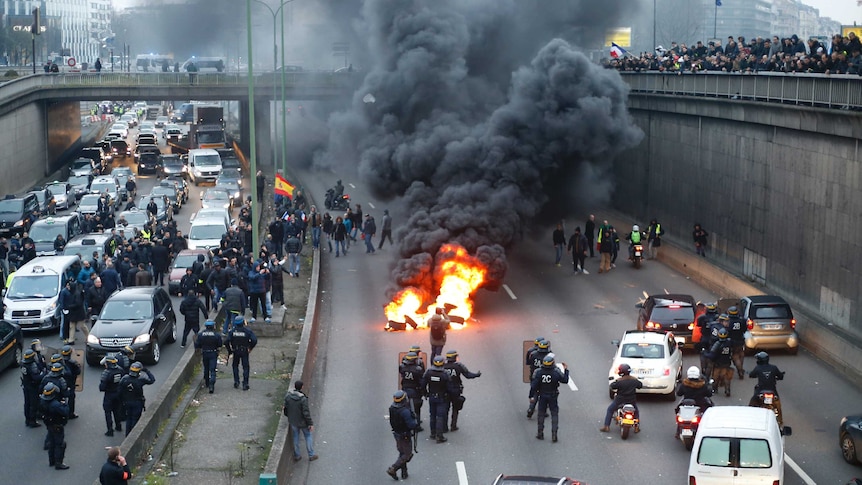 Anti-riot policemen arrive as taxi drivers block the traffic with a fire during a demonstration.