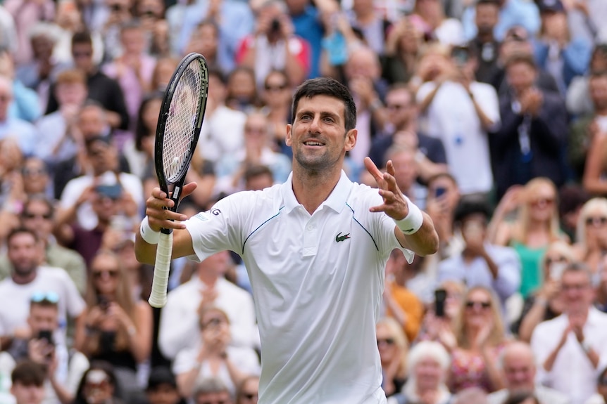 A smiling Novak Djokovic holds his arms out to the crowd in celebration after the final point of his Wimbledon quarter-final.