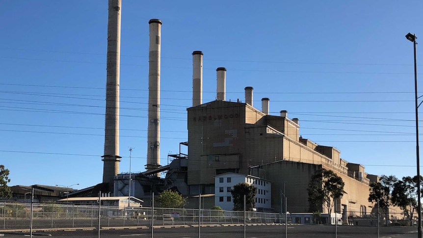 A large power station behind a cyclone fence with eight chimneys