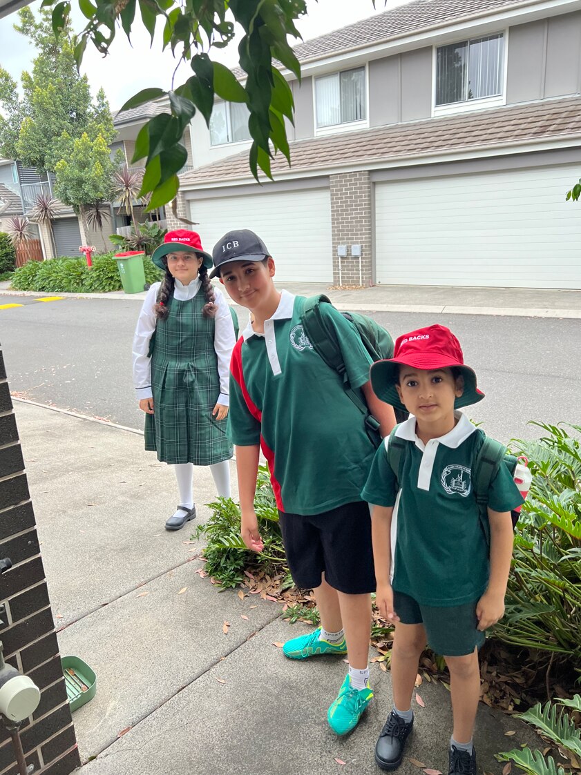 Three young children standing on a footpath in their green school uniforms.