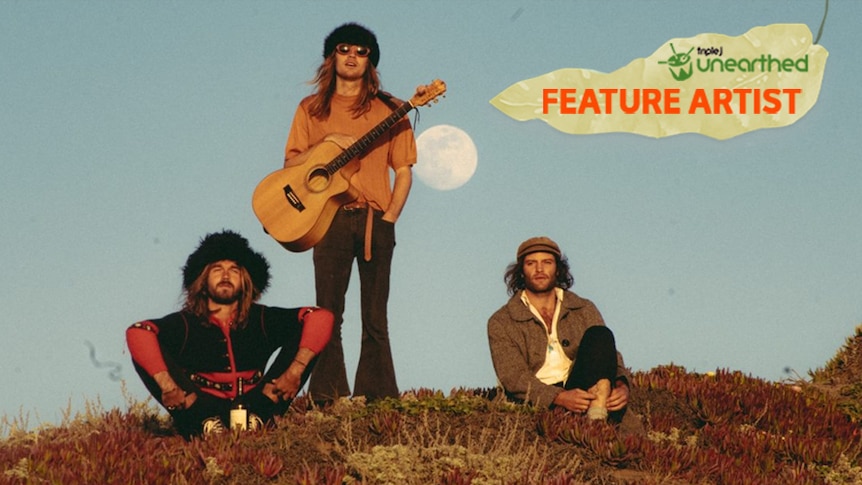 The three members of Le Shiv sit on a grassy hill with the moon behind them and the Feature Artist logo.