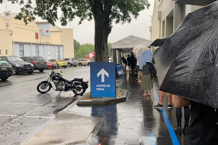 A long line of people in the street with umbrellas waiting for covid testing.
