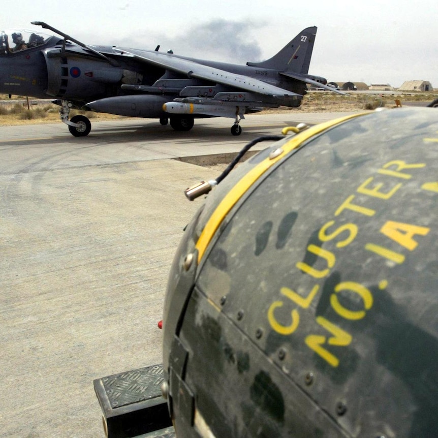 A steely grey fighter plane in the background with the head of a cluster bomb in the foreground