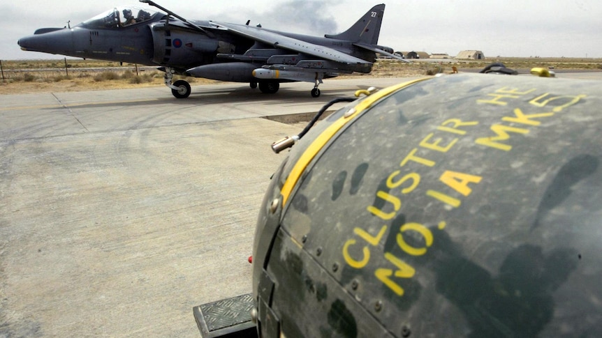 A steely grey fighter plane in the background with the head of a cluster bomb in the foreground