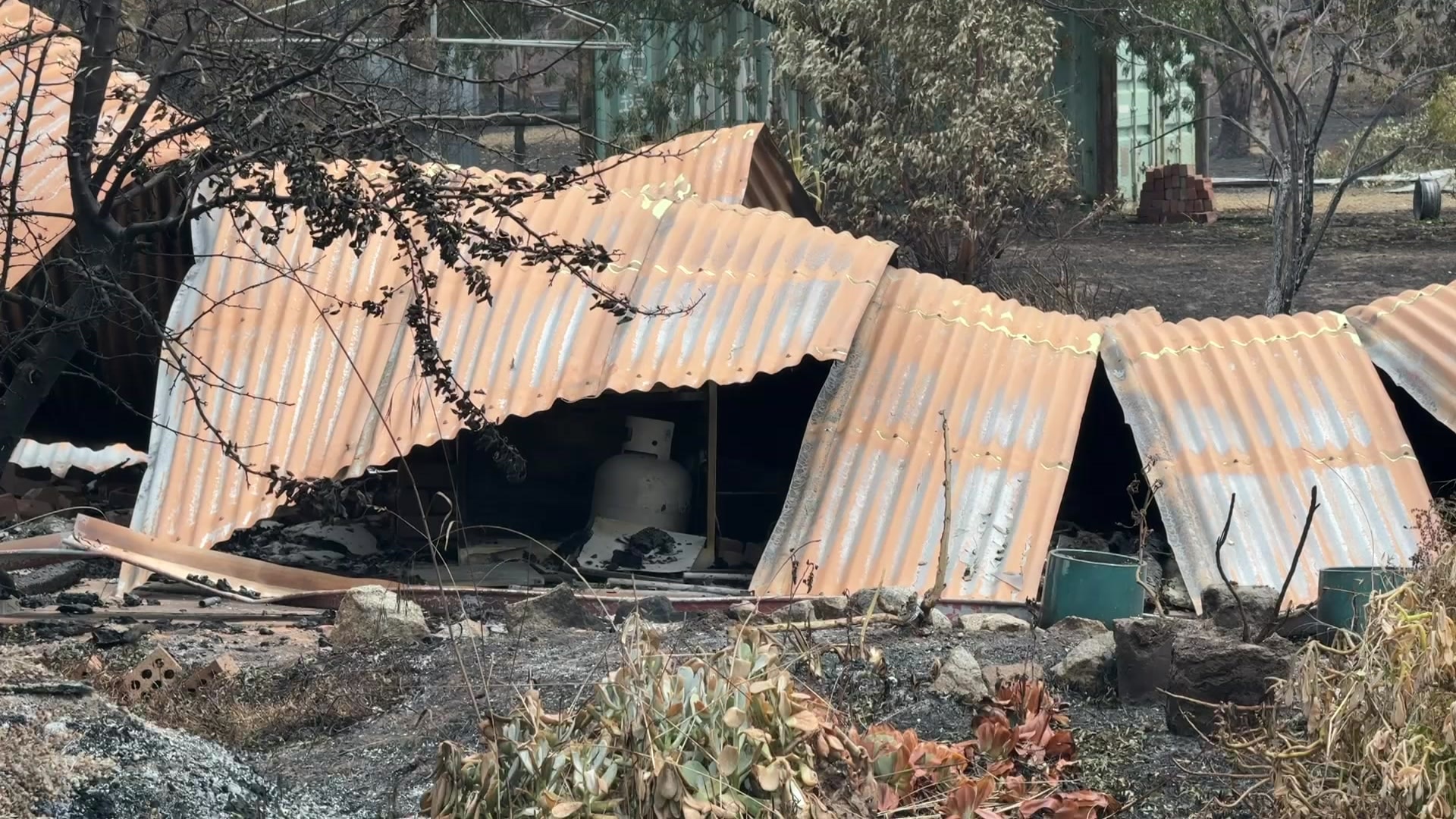 Pedaços de telhado de zinco no chão carbonizado.