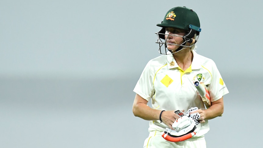 A dejected Beth Mooney walks off the field with her gloves off and bat under her elbow