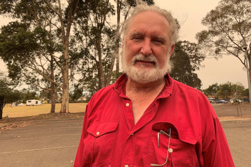 A man stands in a red shirt with a beard
