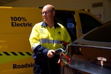 A person wearing a fluro jacket plugs a cord into a Tesla electric vehicle