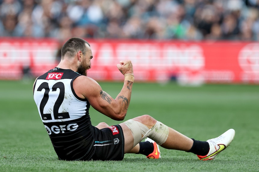 Port Adelaide forward Charlie Dixon sits on the ground and pumps his fist in celebration after kicking a goal during an AFL game