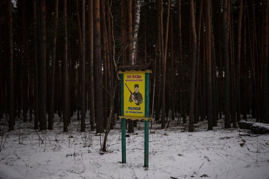 A yellow sign reads "don't be a poacher, hunt by the rules" in a snow-covered forest.