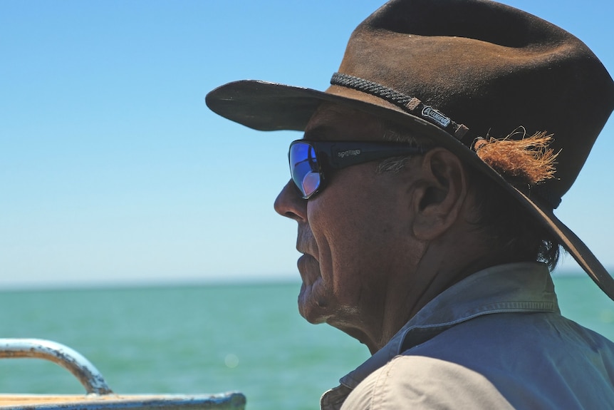 A side profile photo of a man on a boat wearing a hat and sunglasses. 