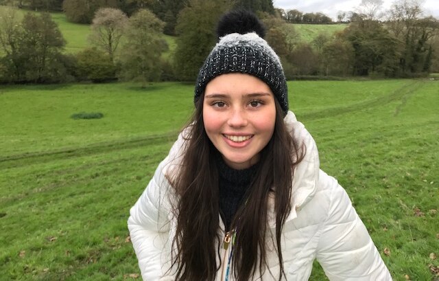 A girl wearing a dark beanie and white jacket smiling for the camera.