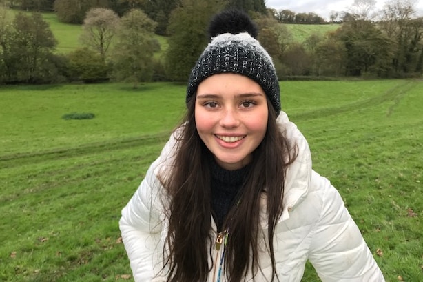 A girl wearing a dark beanie and white jacket smiling for the camera.