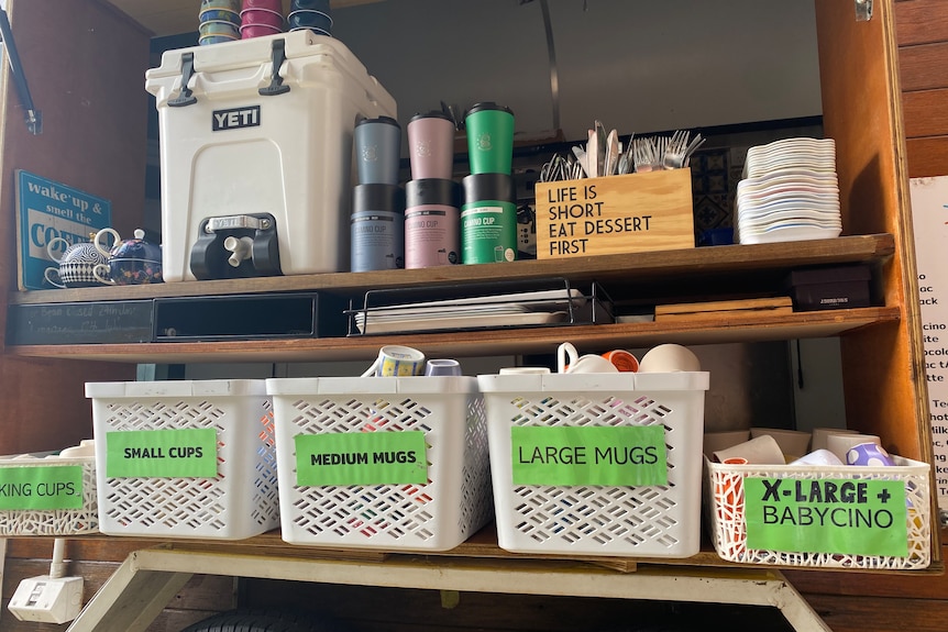 Ceramic mugs and keep cups sit in boxes next to a Yeti cooler.
