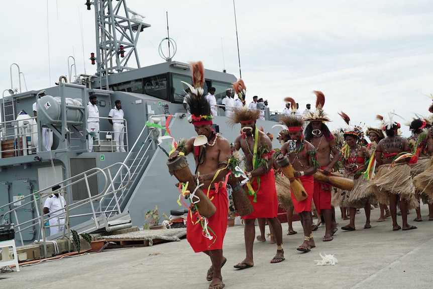 A group of men in traditional Papua New Guinean dress dance in front of an Australian patrol boat