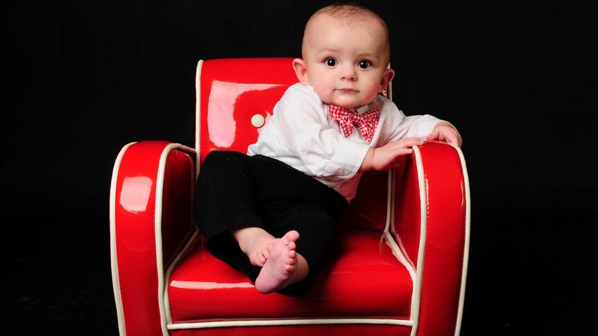 Robbie Buchan, dressed in black pants, white shirt and bow tie, sitting on a red chair.