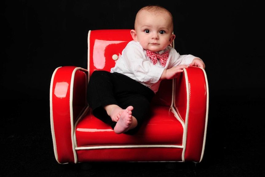 Robbie Buchan, dressed in black pants, white shirt and bow tie, sitting on a red chair.