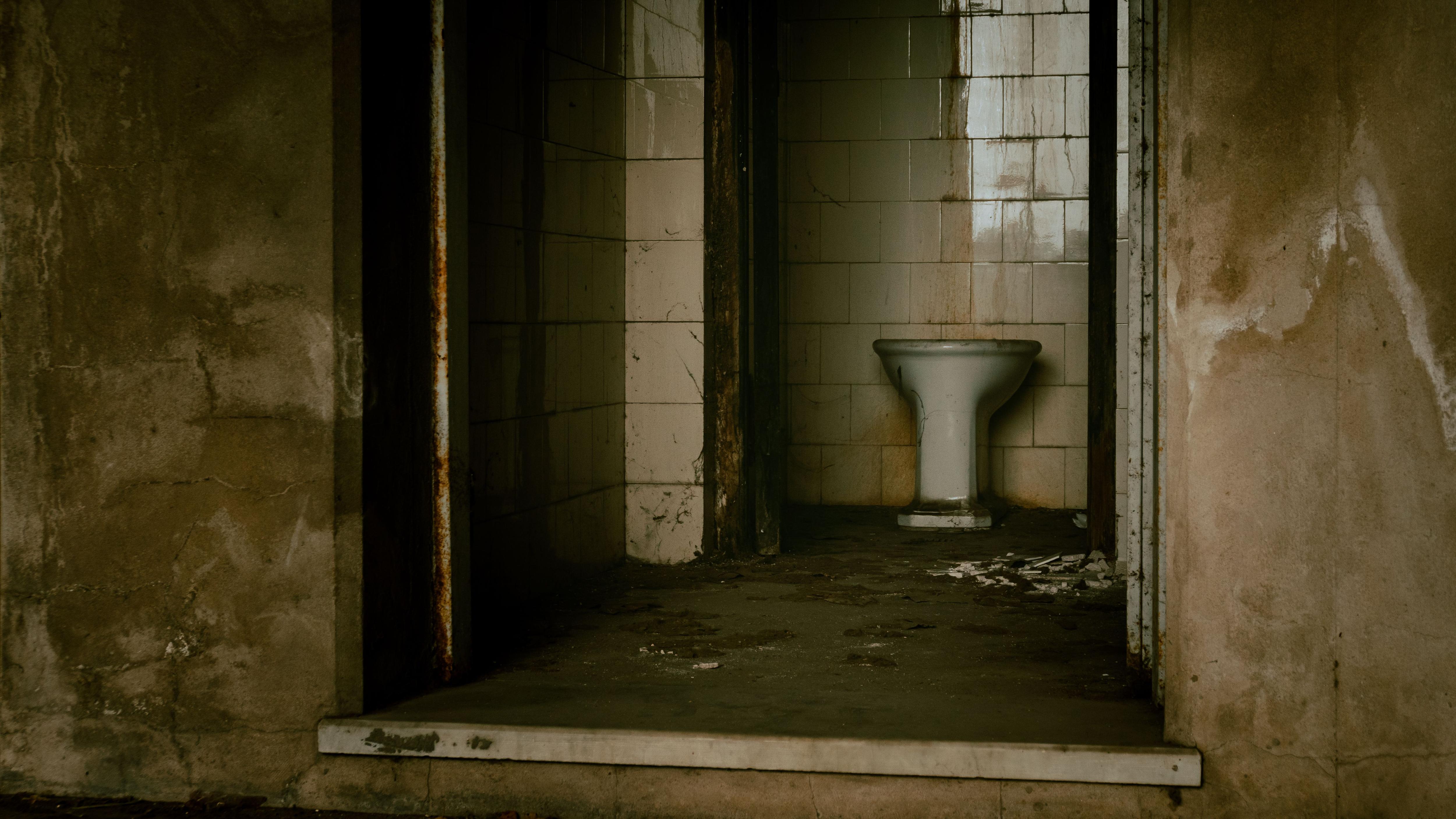 A grimy looking toilet in an abandoned building with debris strewn on the ground